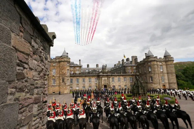 Troops on horseback outside Palace of Holyroodhouse as Red Arrows fly overhead