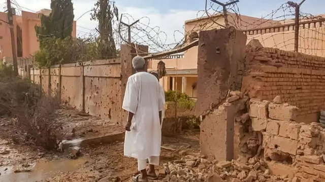 A man walks through rubble by a bullet-riddled wall with barbed-wire, in the aftermath of clashes and bombardment in Omdurman - 4 July 2023