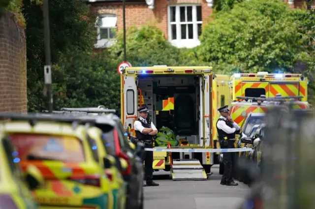 Police officers stand in front of multiple ambulances