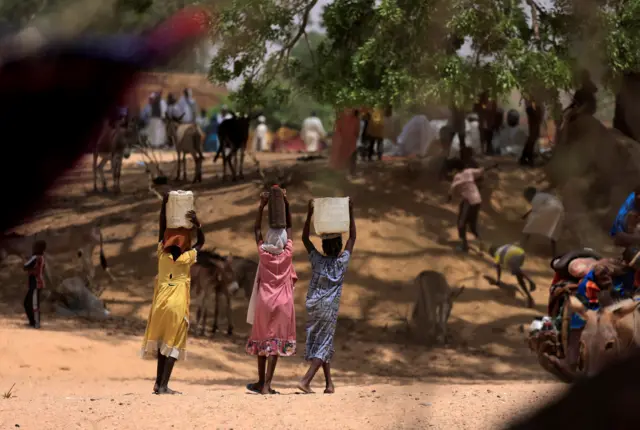 Sudanese women who fled the conflict in Sudan's Darfur region, and were previously internally displaced in Sudan, carry jerrycans of water, near the border between Sudan and Chad, while taking refuge in Borota, Chad, May 13, 2023.