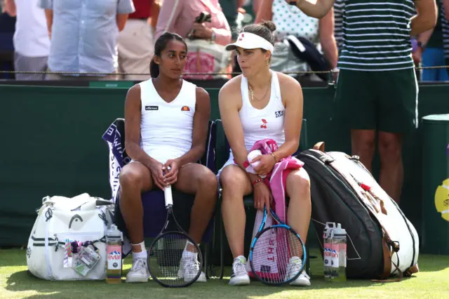 Naiktha Bains and Maia Lumsden sit down at the change of ends