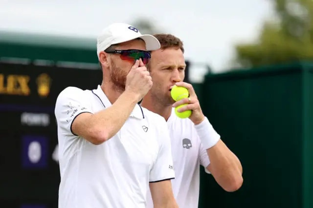 Jamie Murray and Michael Venus cover their mouths while speaking to each other before serving