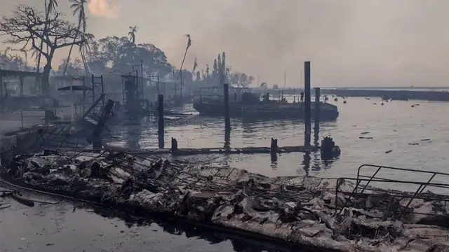 A charred boat sits in the burned waterfront of Lahaina