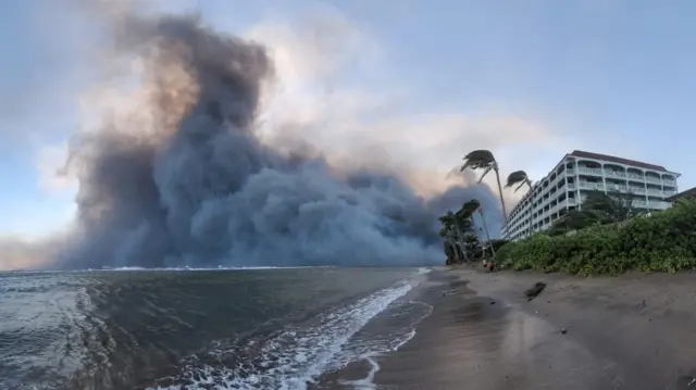 Smoke billows behind a building on a beach