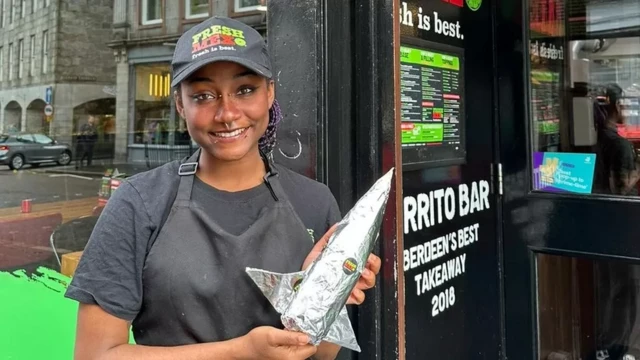 Ana Mayers poses with a burrito in front of a restaurant