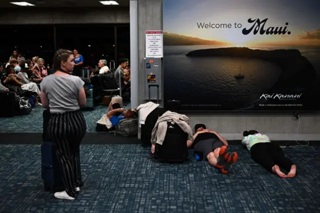 Passengers beneath a "Welcome To Maui" billboard at Kahului airport.