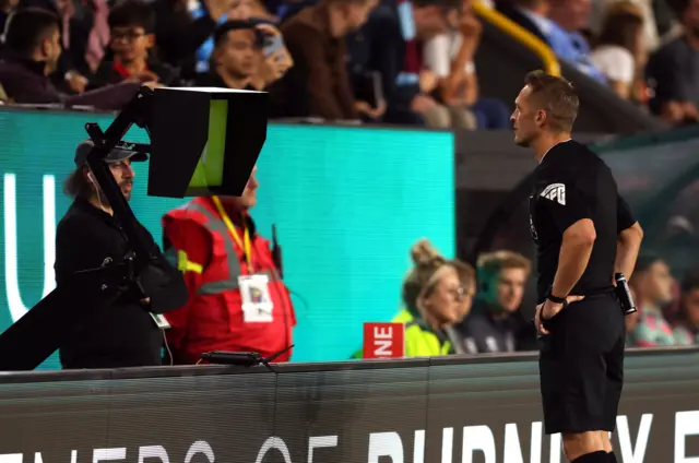 Craig Pawson reviews the Zaroury tackle on the pitchside monitor.