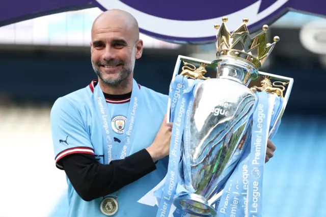 Guardiola holds the Premier Lerague trophy aloft on the stage on the Etihad pitch.