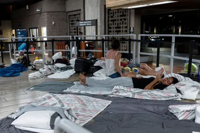 Tourists who were evacuated following wild fire destruction settle for the night as they wait for a flight to leave the island of Maui at the Kahului Airport