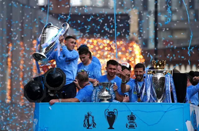 Man City parade their three trophies on a blue open top bus through Manchester.