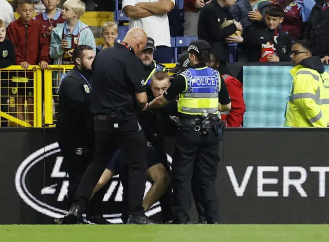 A pitch invader is restrained by police at the side of the pitch.