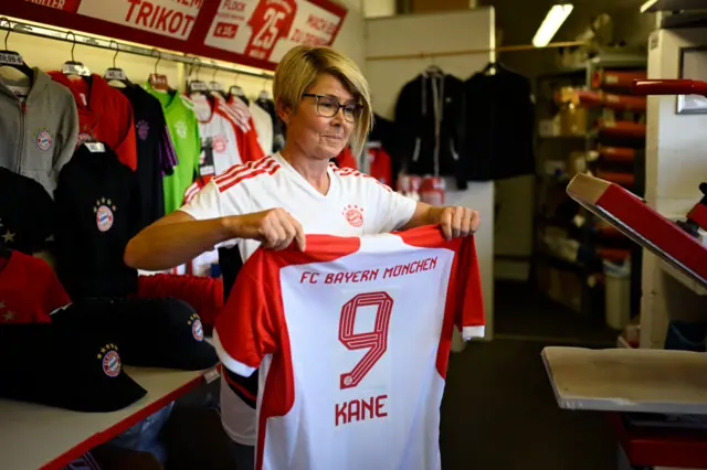 A club shop worker holds up a shrit with the name of Kane newly printed on it.