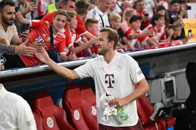 Kane shakes hadns with Bayern fans above the dugout.