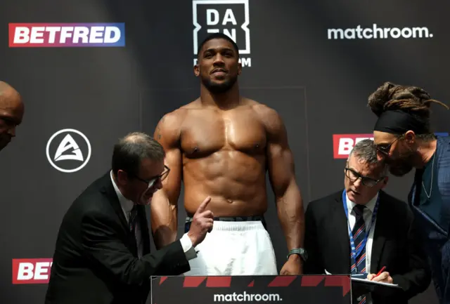 Anthony Joshua stands shirtless on the scales