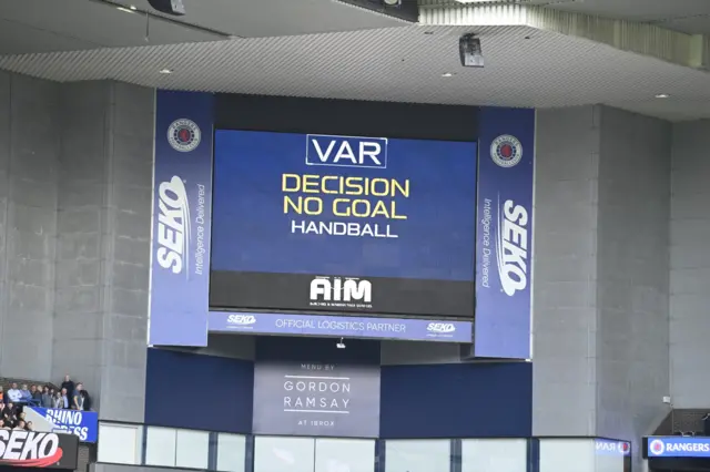 A VAR decision saying 'handball' on a screen at Ibrox