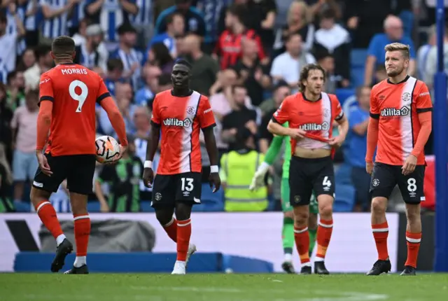 Luton players stand stunned after conceding a fourth goal.