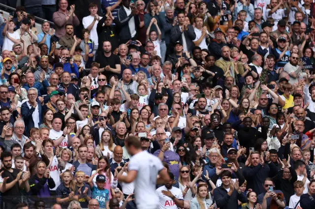 Spurs fans applaud the players as Kane runs down the pitch in the foreground.