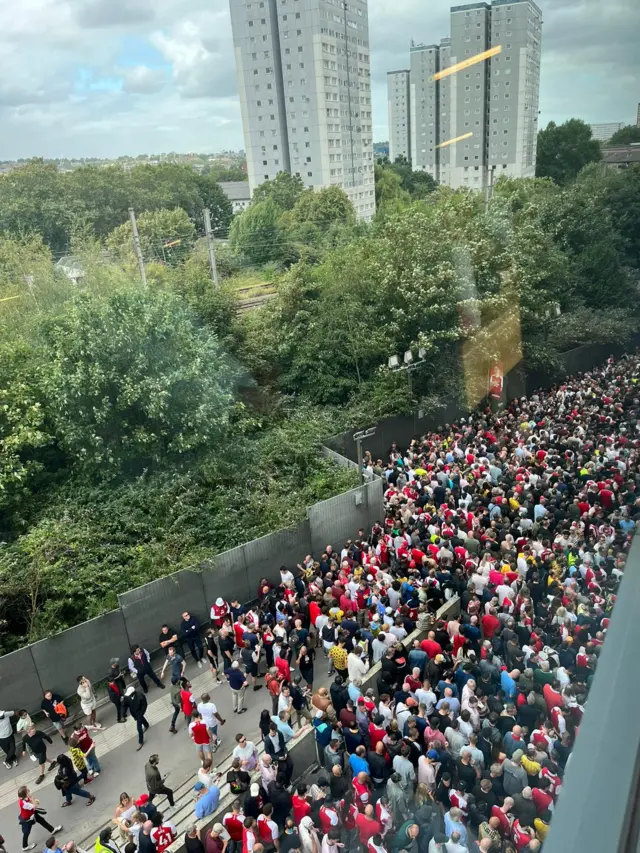 Arsenal fans stand outside the ground unable to get in due to the ticketing system.