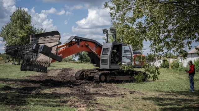 A man holds a remote control in front of an excavator with a demining device attached to it near Kryvyi Rih, Ukraine, on 12 August 2023