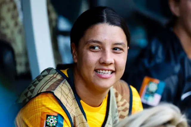 Sam Kerr smiles sat in her place on the bench.