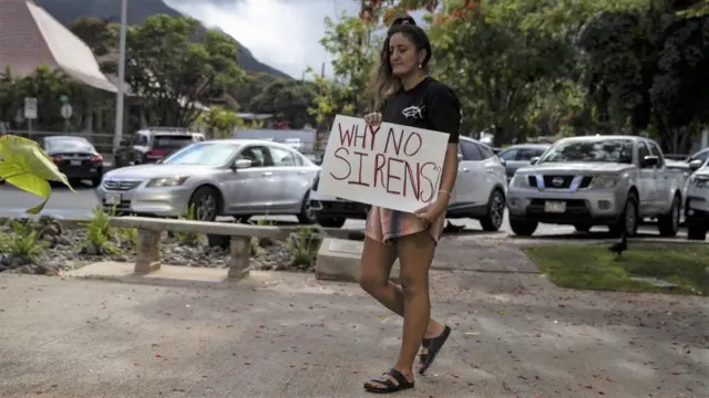 A woman holding a sign asking why no sirens