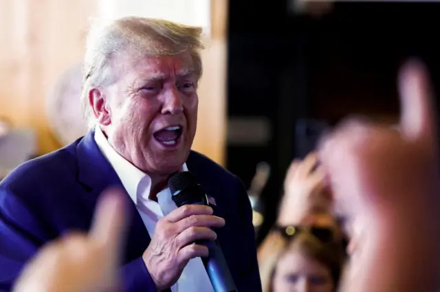 Donald Trump speaking into a microphone, with people around him