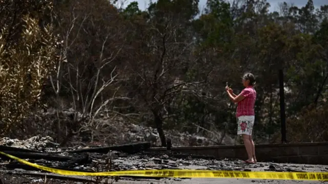 A caretaker photographs the site of a home destroyed by the Maui wildfires in Kula