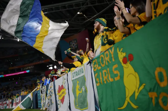 Fans wave flags and banners and cheer on the side as they warm up.