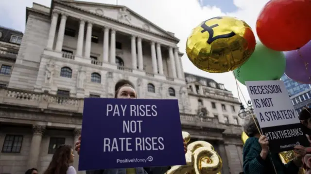 Campaigners from Positive Money protest against interest rate rises outside the Bank of England in London, holding signs that say "pay rises not rate rises" and "recession is not a strategy #taxthebanks"