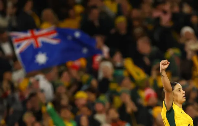 Kerr holds her hand up as a fan waves an Australian flag in the background.