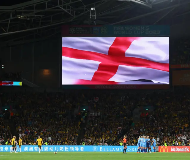 England celebrate while Australia walk b ack to kick off, the big screen flies the England flag after their goal.