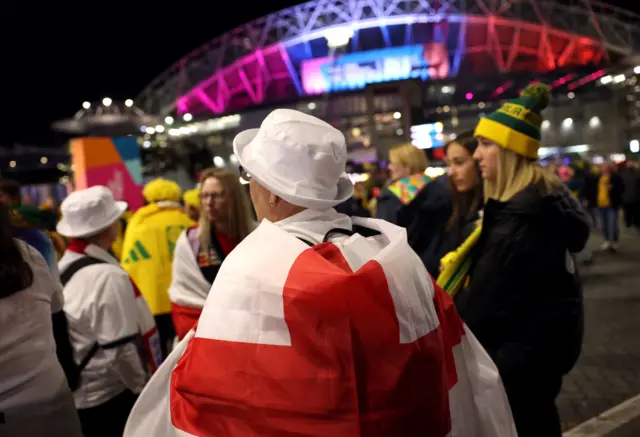 An England fan with a bucket hat stood in front of a group of Matildas fans.