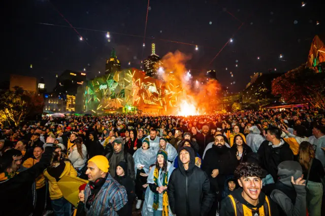 A sea of Australian fans stand in a fan park watching the game.