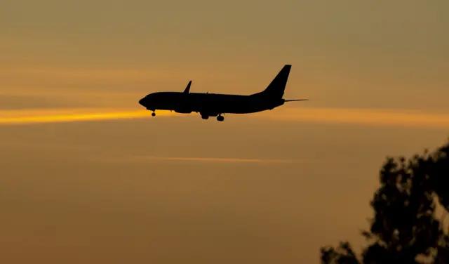 A silhouette of a passenger plane flying against a sunset