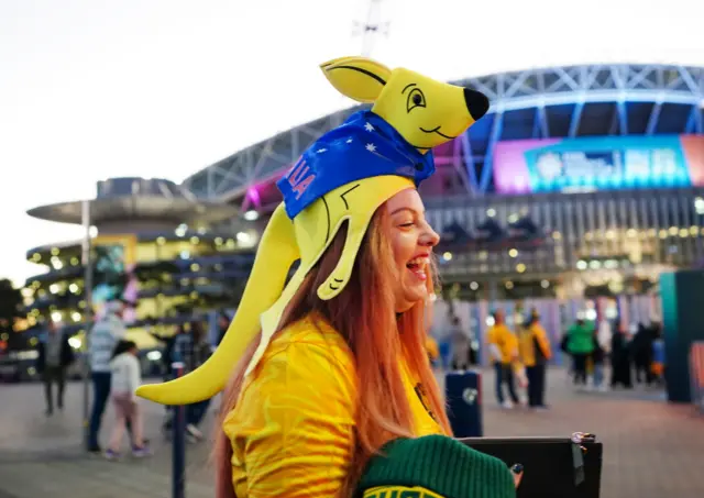 A fan has a kangaroo hat on outside the ground.