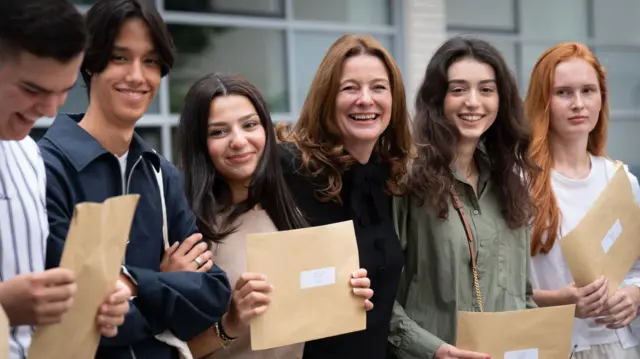 A group of students holding their exam results while standing with Education Secretary Gillian Keegan