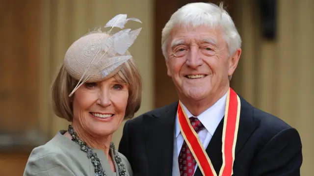 Sir Michael Parkinson accompanied by his wife Lady Mary Parkinson after receiving his Knighthood from Queen Elizabeth II at Buckingham Palace, London.