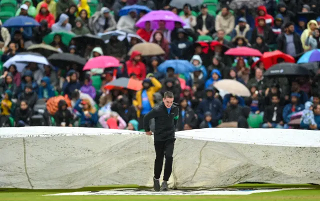 A member of the ground staff helps to bring on the covers