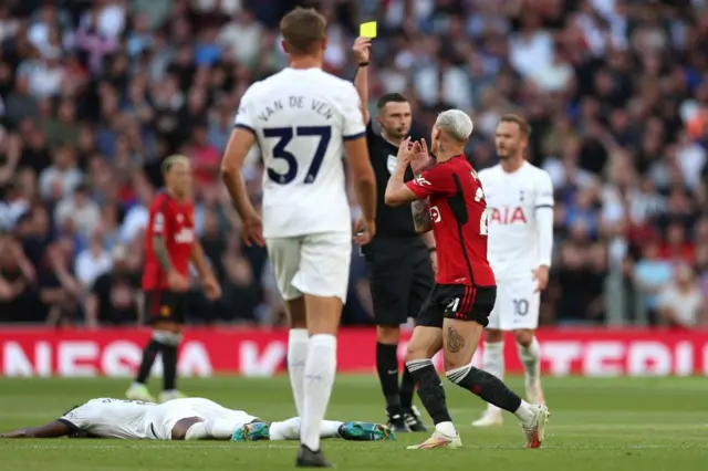 Antony holds his hand to his head as he is shown a yellow card by the referee.