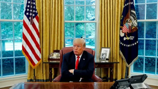 Donald Trump behind a desk in the Oval Office, White House.