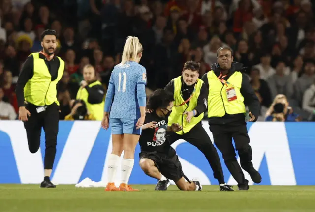 A pitch invader is tackled by security in front of Hemp.