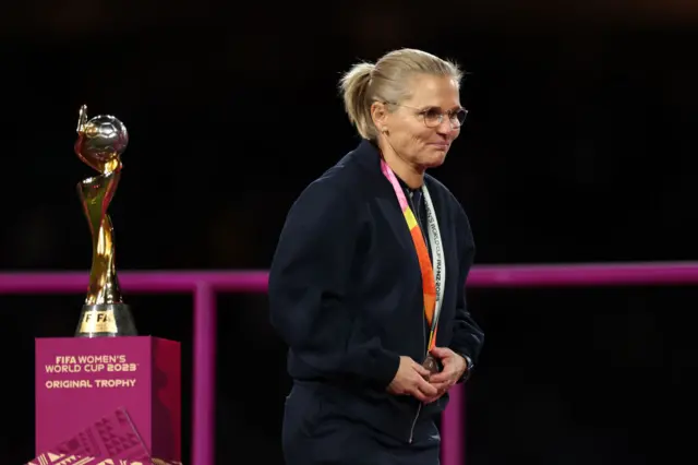 Sarina Wiegman walks past the trophy.