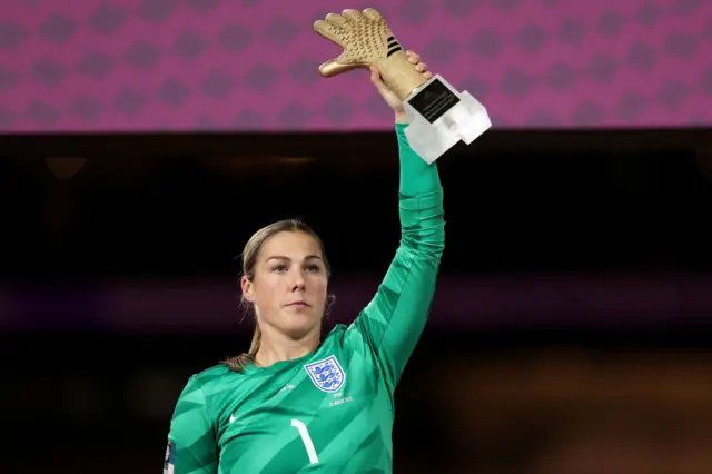 Mary Earps holds her golden glove award aloft.