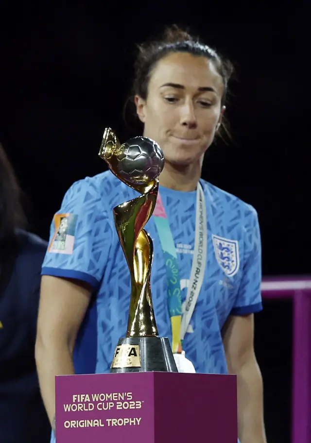 Lucy Bronze stares at the World Cup trophy as she walks past with her runners up medal.