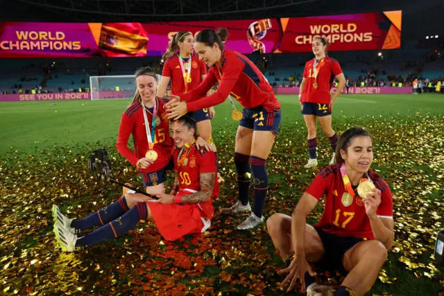 Spain players celebrate with their gold medals on the pitch surrounded by gold ticker tape.