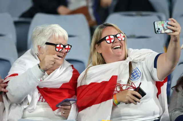 England fans with shirts, flags and glasses take a selfie in their seats.