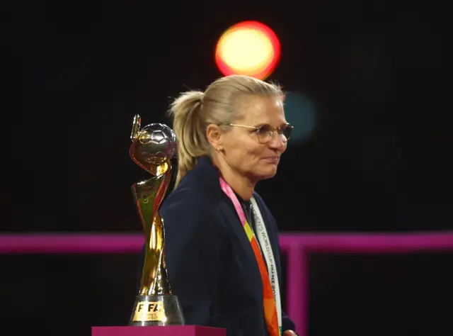 Sarina Wiegman walks past the trophy with her runners up medal.