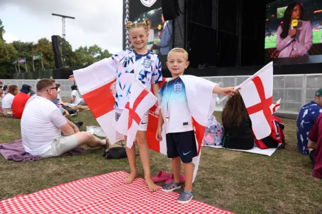 Two young fans wave England fans in front of a big screen.