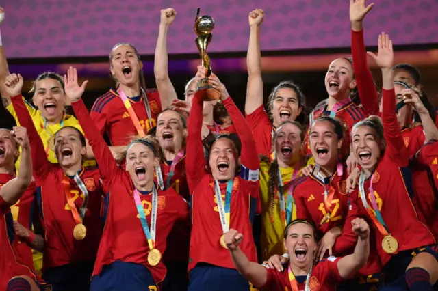 Ivana Andres lifts the world cup trophy surrounded by her Spain teammates.