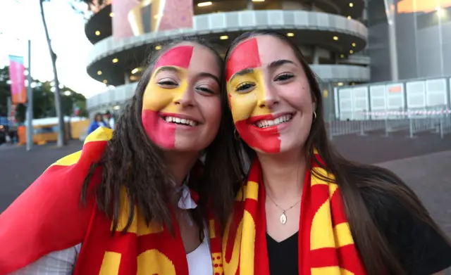 Spain fans with scarves and face paint arrive at the stadium.